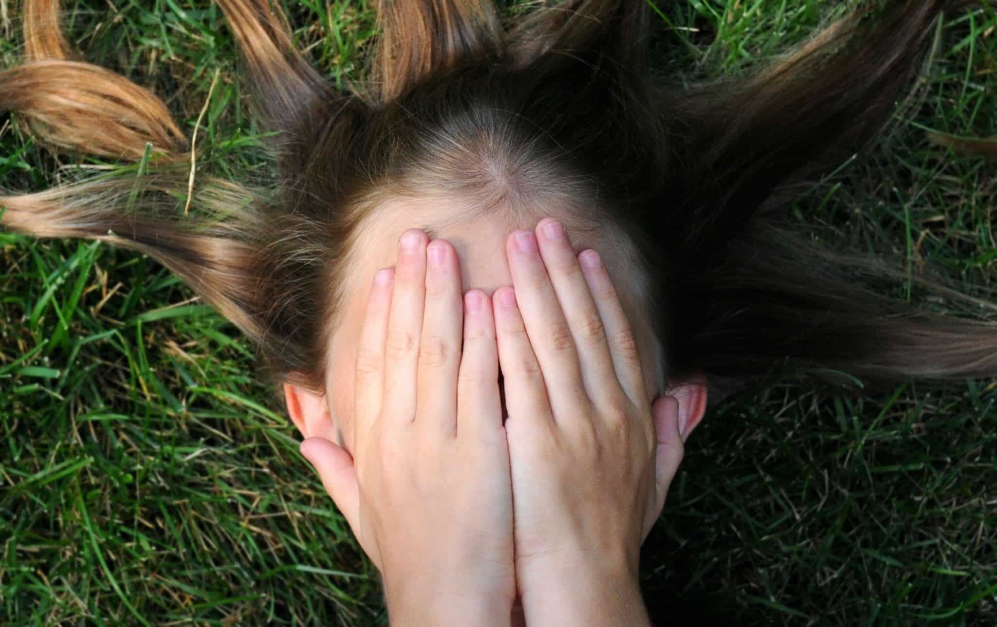 woman covering her face lying on green grass