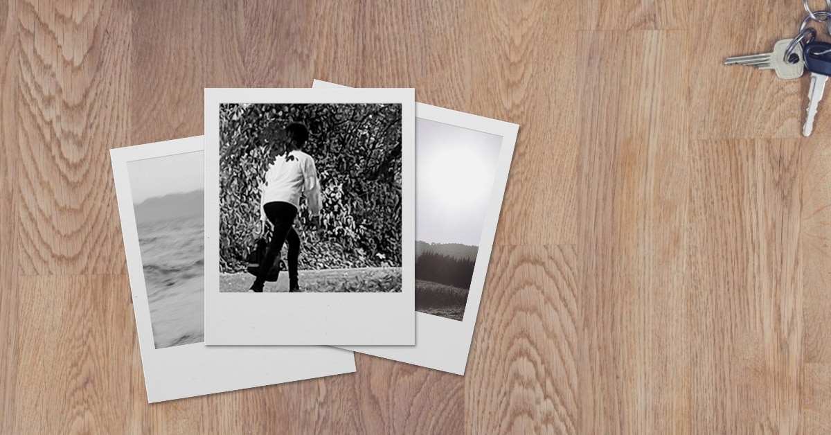 3 black and white polaroid photos stacked on a desk. The bottom photos are barely visible and of landscapes. The top photo is of a young person in black pants and a white shirt walking away.