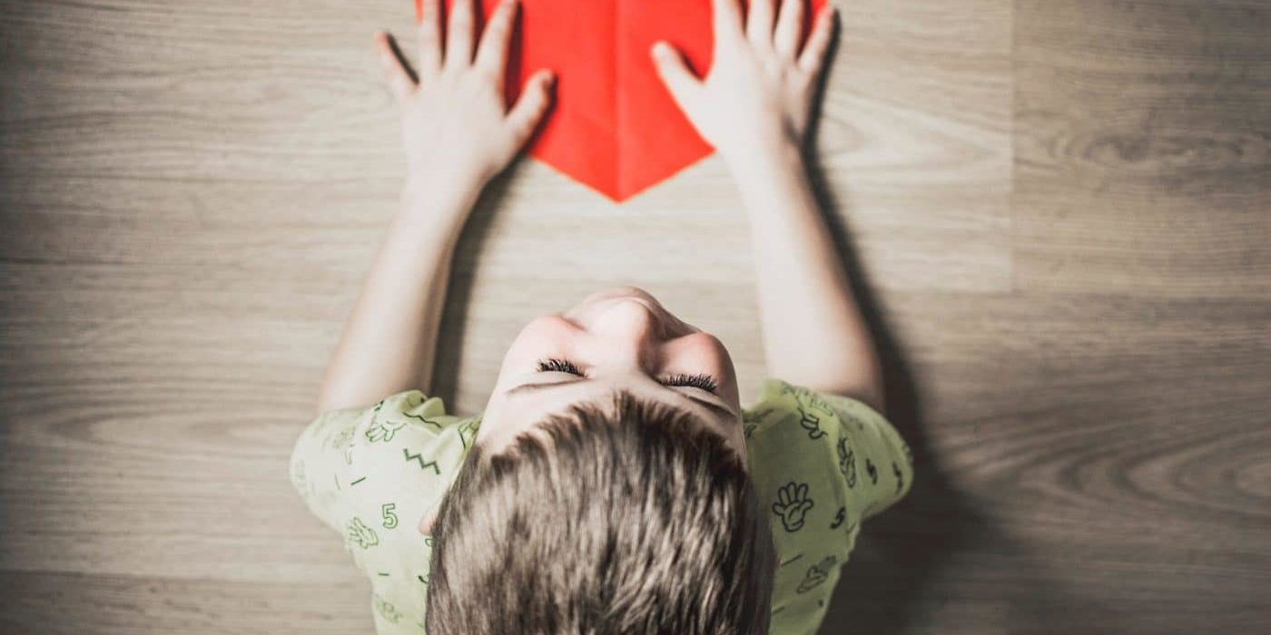 boy in green shirt holding red paper heart cutout on brown table