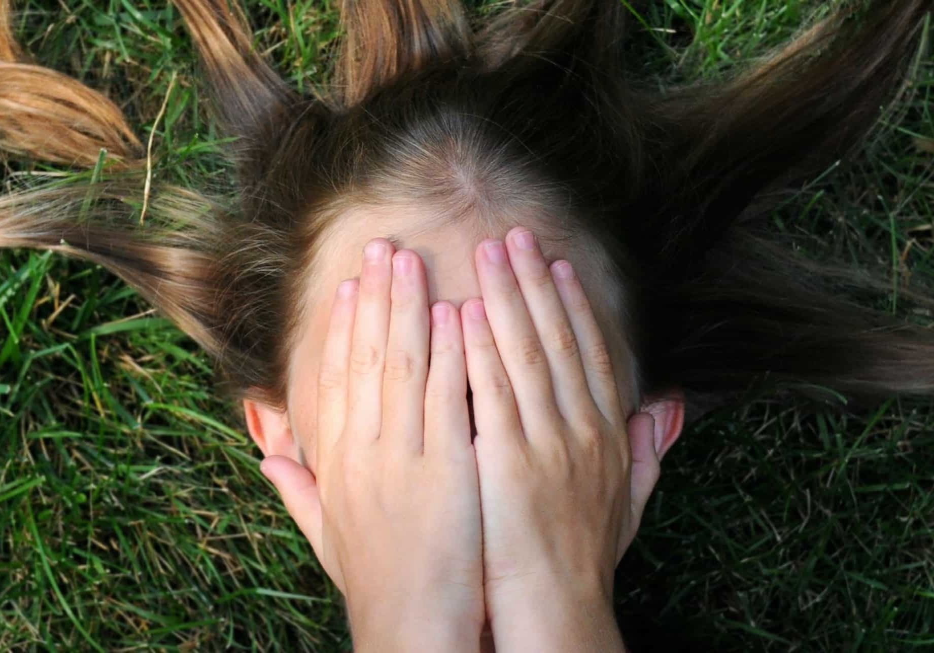 woman covering her face lying on green grass