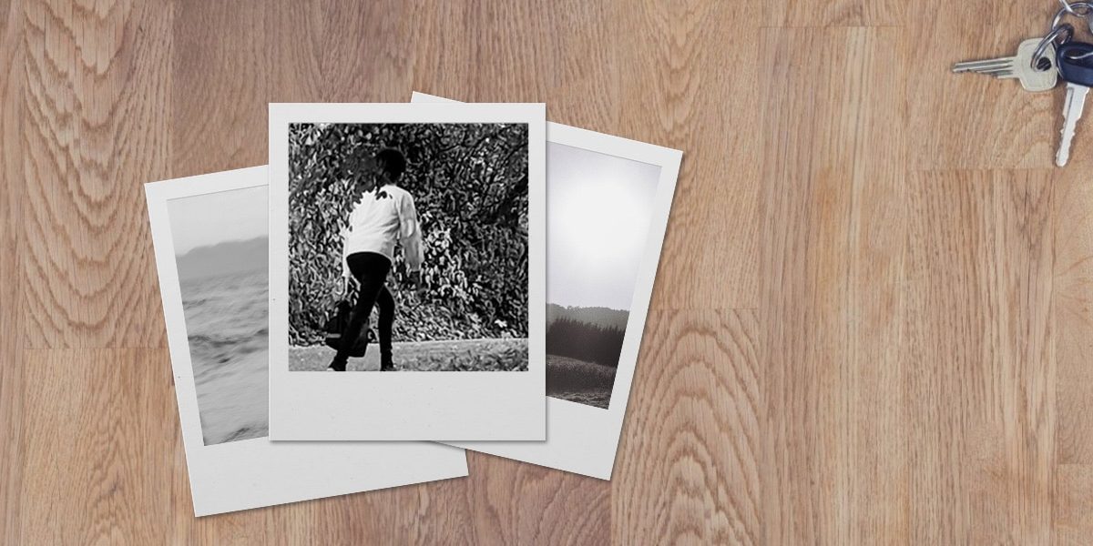 3 black and white polaroid photos stacked on a desk. The bottom photos are barely visible and of landscapes. The top photo is of a young person in black pants and a white shirt walking away.